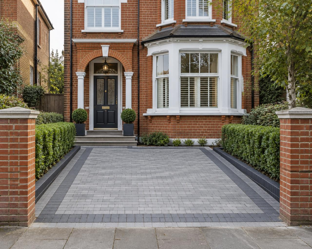 Block-paved front driveway framed by clipped hedges and brick piers
